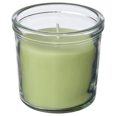 Une bougie verte parfumée LÖVSKOGSLUND dans un bocal en verre transparent, à base de plantes et de cire de paraffine, avec une mèche en coton.