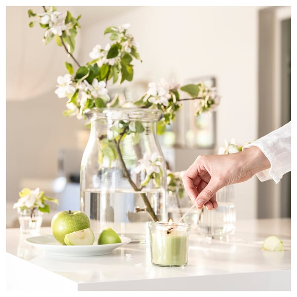 Bougie verte allumée à côté d’un vase à fleurs blanches, pommes sur une table en marbre.