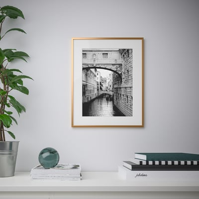 Cadre photo sur le mur affichant une photo de pont en noir et blanc, entourée d’une plante, de livres et d’un orbe décoratif.