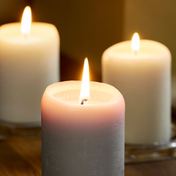 Trois bougies allumées dans des tons blancs, roses et gris projetaient une lueur douillette sur une surface en bois.