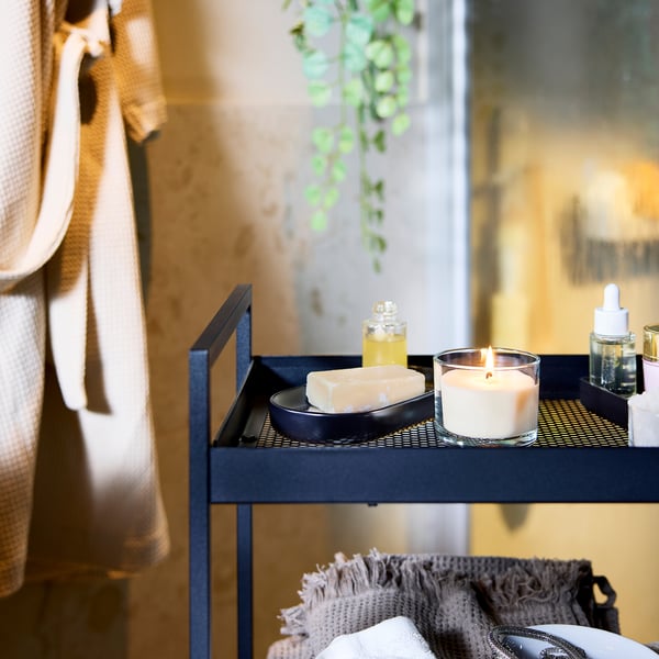 Un plateau en métal gris contient une bougie blanche, des barres de savon, un compte-gouttes d’huile et de petites plantes.