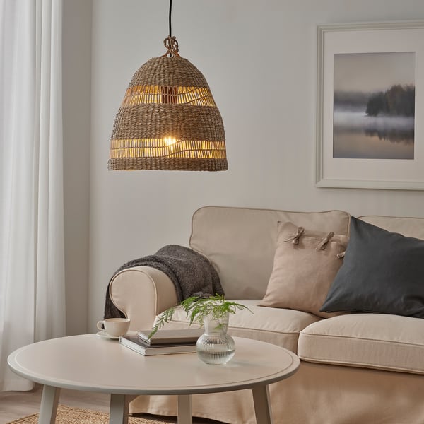 Salon confortable avec canapé beige, couvertures et table basse avec des livres et de la verdure. L’éclairage chaleureux comprend une lampe et une ampoule LUNNOM.