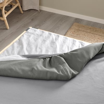 Une base de lit à paquet plat avec une housse amovible et des pieds en bois posés sur un sol en bois.
