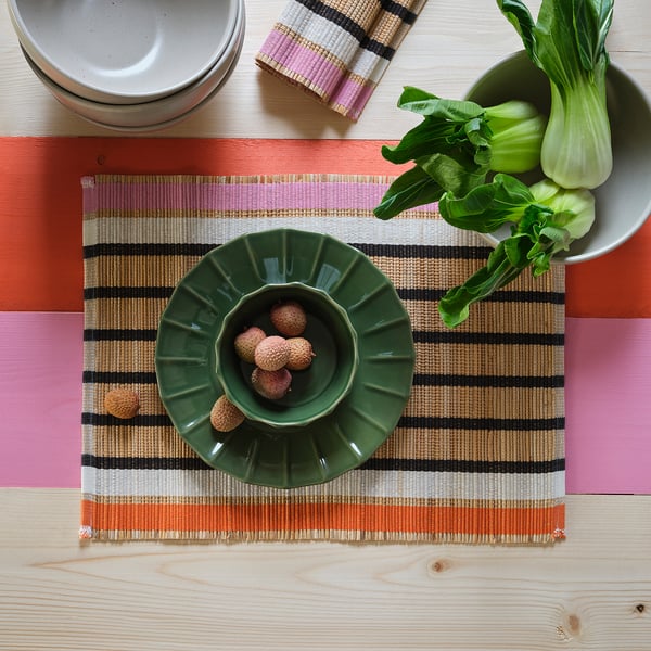 Table dressée avec natte tissée, bol vert de litchis et bok choy sur un plateau.