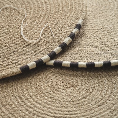 Set de table rond en jute naturel MÄVINN avec bordure noire et blanche.