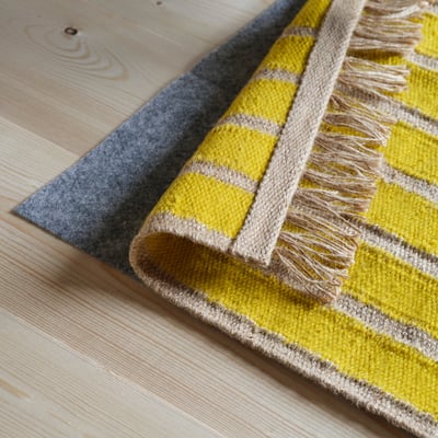 Tapis rayé jaune et beige avec franges sur parquet.