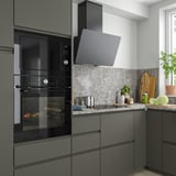 Cuisine moderne avec four noir MÅGEBO et micro-ondes. Les armoires sont assorties aux appareils. Le comptoir a un évier, des plantes et des légumes.