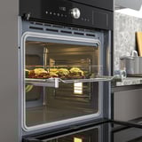 Four moderne avec porte ouverte montrant un plat de légumes rôtis ; A 5 niveaux, chaleur ventilée, cuisson à la vapeur pour les aliments humides.