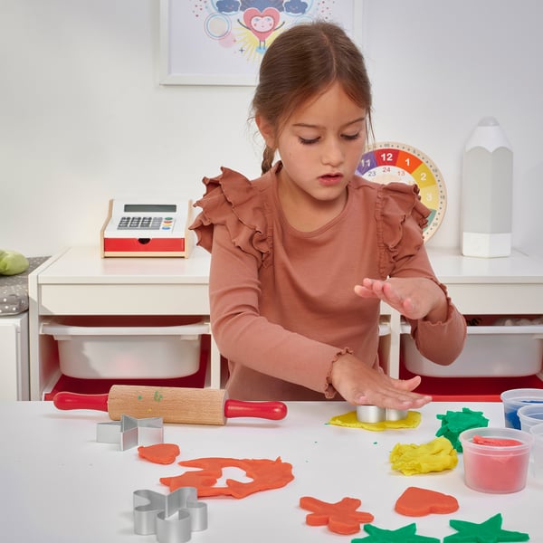 Une jeune fille joue avec la pâte à modeler MÅLA, découpant des formes avec des emporte-pièces inclus, à l’aide d’un rouleau à pâtisserie.