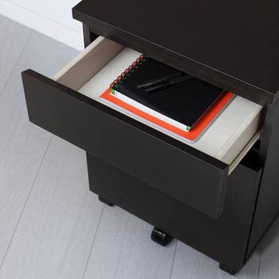 Table de chevet MALM noire avec tiroir ouvert montrant cahier et stylos, roulettes pour un déplacement facile.