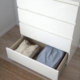 Commode blanche ouverte avec parquet, montrant les vêtements bien rangés dans les tiroirs.