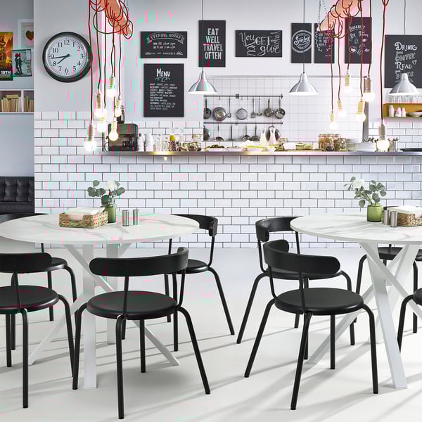 Café moderne avec des tables MARIEDAMM : chaises noires élégantes, plateaux de table circulaires, pieds entrecroisés en métal robuste. Design lumineux, confortable et minimaliste.