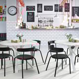 Café moderne avec des tables MARIEDAMM : chaises noires élégantes, plateaux de table circulaires, pieds entrecroisés en métal robuste. Design lumineux, confortable et minimaliste.