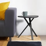 Table d’appoint grise moderne avec des pieds entrecroisés à côté d’un fauteuil.