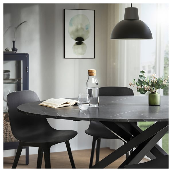 Ensemble de salle à manger noir moderne avec table ovale, quatre chaises et lampe suspendue.