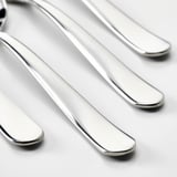 Quatre cuillères métalliques brillantes, propres et polies, posées parallèlement sur une surface blanche.
