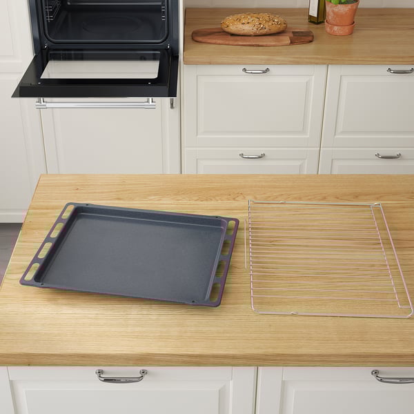 Scène de cuisine avec plaque de cuisson noire et grille sur un comptoir en bois près d’un four ouvert, suggérant une préparation pour la cuisson.