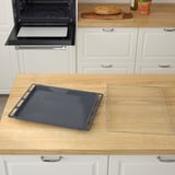 Une plaque de cuisson et une grille noires reposent sur un comptoir en bois près d’un four ouvert avec des armoires blanches.