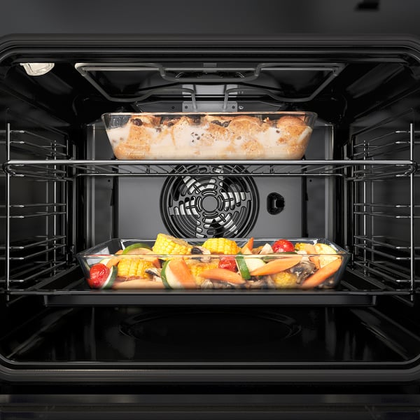 Intérieur du four à convection forcée par ventilateur, montrant deux plats : une cocotte et des légumes.