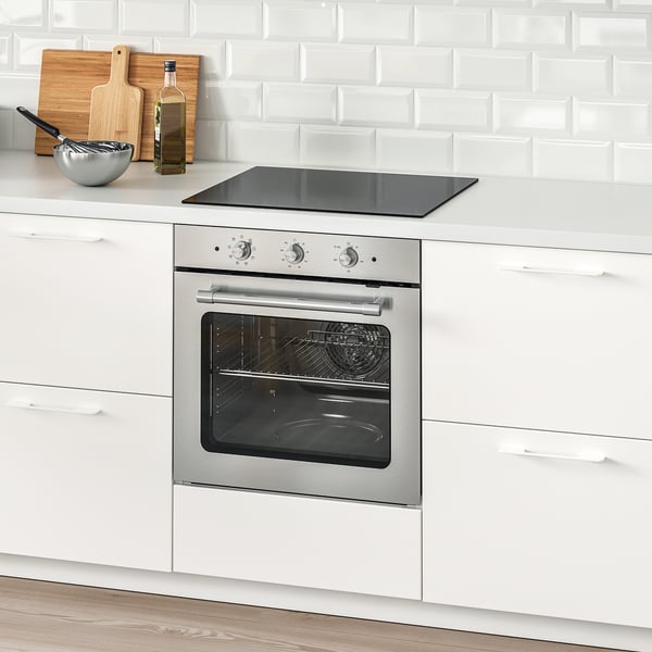 Cuisine moderne avec four en acier inoxydable, armoires blanches, dosseret en céramique.