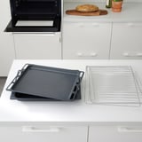 Mitaines de cuisine noires sur comptoir blanc. À proximité, des plaques de cuisson noires et des grilles de refroidissement se trouvent à côté du pain sur une planche à découper.