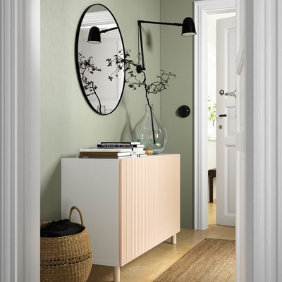 Salon moderne avec buffet MEJARP, miroir, lampes et panier de vêtements contre mur végétal.