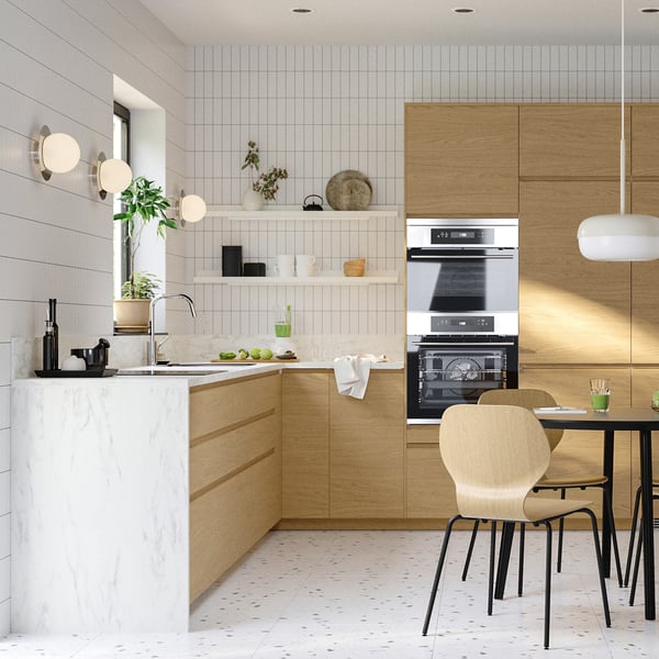 Cuisine moderne avec armoires en chêne, comptoir en marbre blanc, four encastré et chaises de salle à manger en bois.