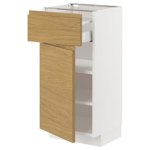 Un meuble de cuisine METOD blanc avec un tiroir et une porte en chêne clair, partiellement ouvert, révélant un espace de rangement à l’intérieur.