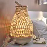 Une lampe MISTERHULT avec un cadre en bambou beige naturel, dotée d’une lumière chaude et rougeoyante, posée sur une table de chevet.