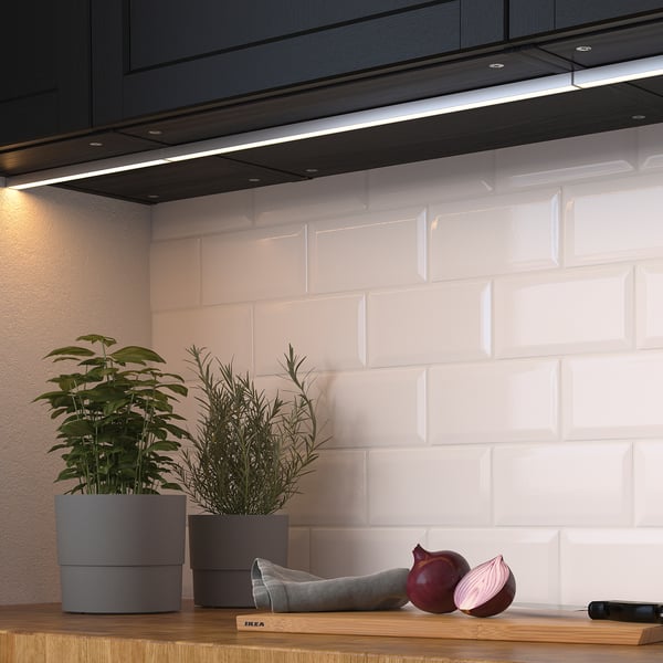 Cuisine moderne avec des lumières led sous les armoires, mettant en valeur les plantes et les oignons sur un comptoir en bois.