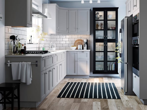 Cuisine moderne avec des armoires grises, des appareils électroménagers en acier inoxydable, un tapis noir et des suspensions blanches MITTLED.