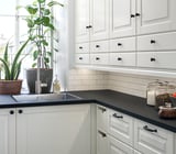 Cuisine moderne avec des armoires blanches, des comptoirs noirs et une plante en pot près d’une fenêtre. Équipé de luminaires MITTLED.