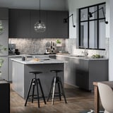 Cuisine moderne avec luminaire MITTLED. Il s’agit d’armoires grises, d’un comptoir en marbre et de tabourets noirs.