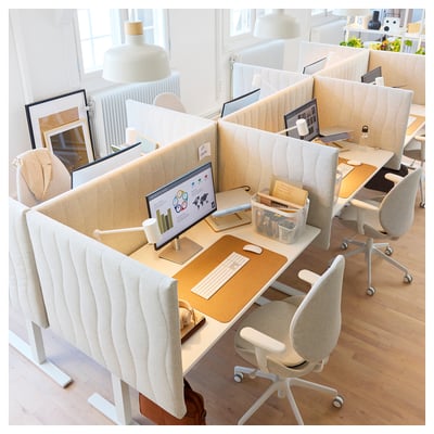 Configuration de bureau moderne avec des bureaux beige, des chaises blanches et des écrans de séparation. Ordinateurs et accessoires organisés sur des planchers en bois de couleur claire.