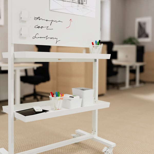 Unité mobile blanche avec des étagères, des marqueurs et une tablette. Comprend un tableau blanc avec des notes manuscrites, dans un bureau.