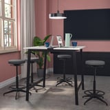 Table de conférence MITTZON avec tabourets, noire avec plateau blanc, contre mur rose, espace de travail avec technologie, fenêtre.