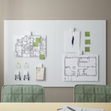Un tableau blanc avec un cadre vert et des chaises vertes. Le tableau affiche des plans architecturaux et des post-it colorés, mettant en évidence la configuration d’un espace de travail.