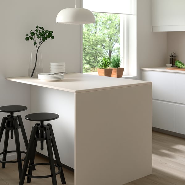 Îlot de cuisine moderne avec plateau en porcelaine MÖCKLARP blanc, tabourets, assiettes et verdure noirs.