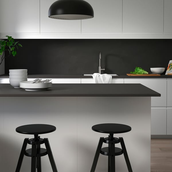 Cuisine moderne avec comptoir noir, tabourets, évier, armoires grises et suspension.