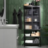 Salle de bain carrelée vert foncé avec armoire à mousse, serviettes et plantes.