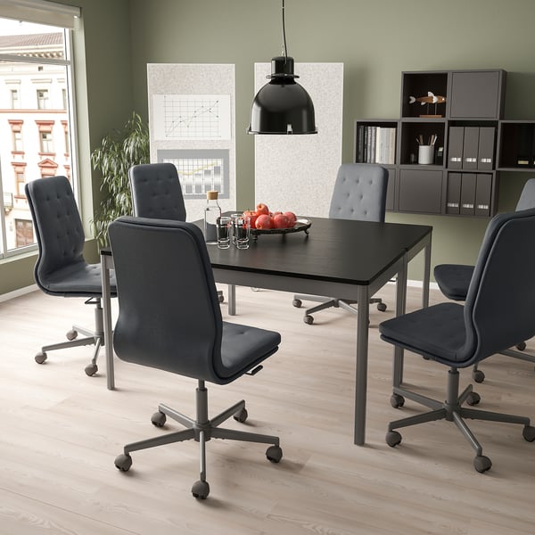 Configuration de bureau moderne avec des chaises MULLFJÄLLET grises autour d’une table noire, d’une suspension noire, d’un mur vert. Grande fenêtre avec vue sur la ville.