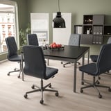 Configuration de bureau moderne avec des chaises MULLFJÄLLET grises autour d’une table noire, d’une suspension noire, d’un mur vert. Grande fenêtre avec vue sur la ville.