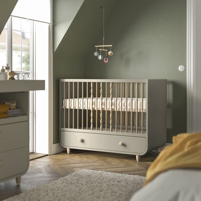 Pépinière moderne avec murs végétaux. Lit bébé MYLLRA gris et couleur bois, plus petit que la commode voisine, avec mobile au-dessus.
