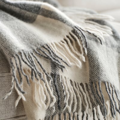 Un plaid en laine MYRULL gris clair et blanc à motif à carreaux, avec des bords frangés.
