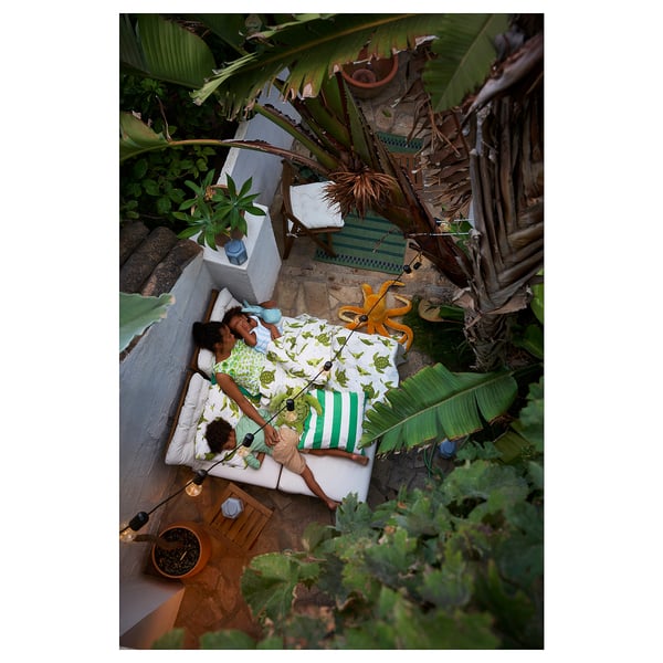 Deux personnes se détendent sur un patio tropical à la verdure luxuriante et aux tapis NÄMMARÖ.