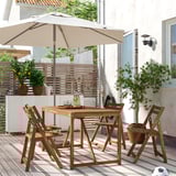 Ensemble de patio en bois avec parasol sur la terrasse. Quatre chaises, des plantes et une maison en arrière-plan.