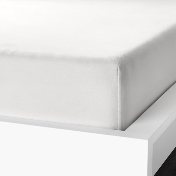 Coin du drap de lit blanc exposé, mettant en valeur la flanelle de coton douce et veloutée et la bordure élastique pour un ajustement sûr.