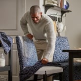 Homme posant une housse de chaise florale bleue sur une chaise à assise blanche.
