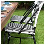 Deux chaises tissées noires et blanches à côté d’une table en bois d’extérieur garnie de vaisselle et de verres bleus.