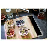 Planche à découper de cuisine en bois avec des bols de fruits et de granola sur un comptoir sombre.